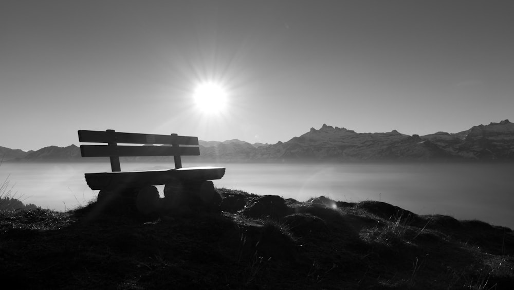 grayscale photo of bench on rock formation near body of water