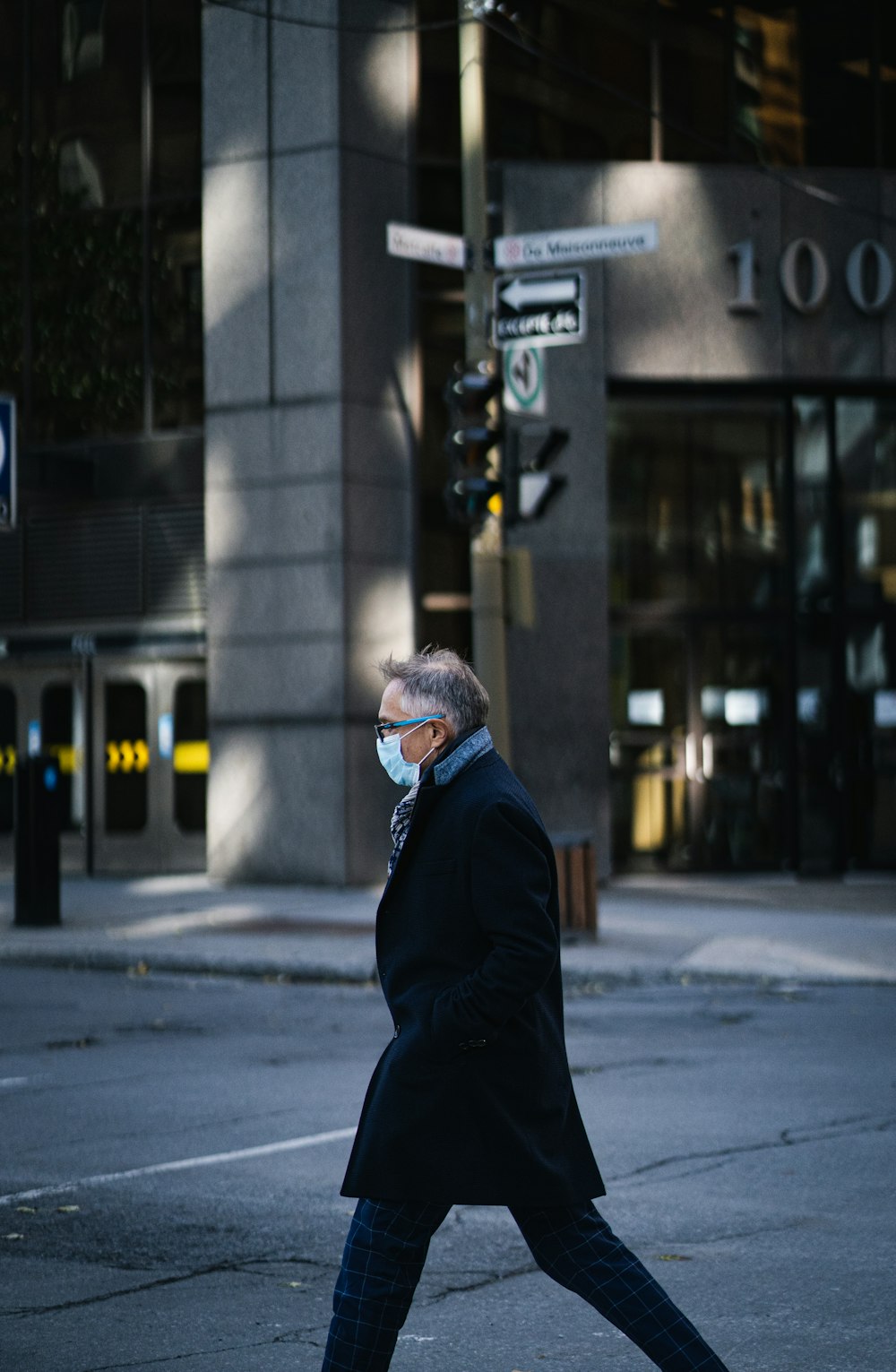 白と青のニット帽をかぶった黒いジャケットを着た男性が昼間、建物の近くに立っている