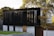 A modern building with a sleek design featuring dark, reflective panels and large, vertical window shades. The structure is surrounded by a well-maintained lawn and a few trees, and the sun casts soft shadows, highlighting the architectural lines.