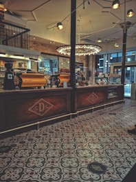 Interior view of Ambos Mundos coffee & bakery with soft beige and brown decor, rounded edges, and warm lighting highlighting a barista serving coffee.