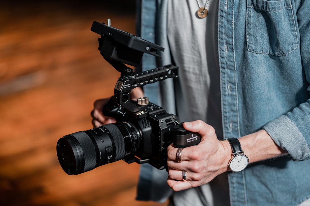 person in blue denim jacket holding black dslr camera