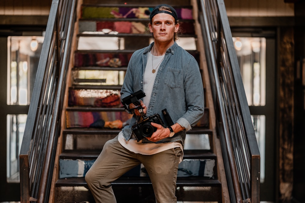 man in blue denim jacket and brown pants holding black dslr camera