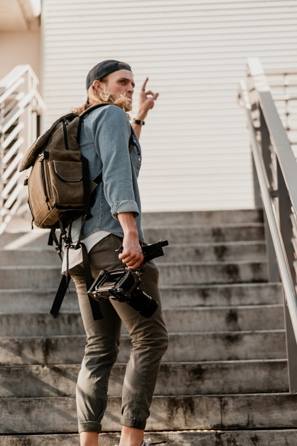 man in blue dress shirt and brown pants with black backpack walking on stairs during daytime