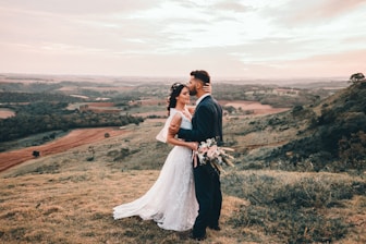 man and woman kissing on brown grass field during daytime