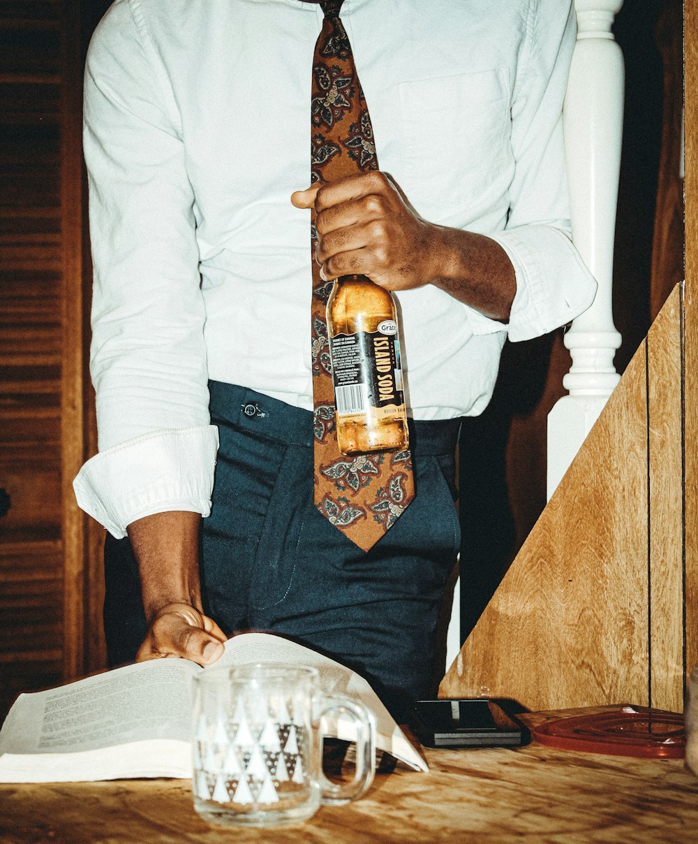 man in white long sleeve shirt holding brown glass bottle
