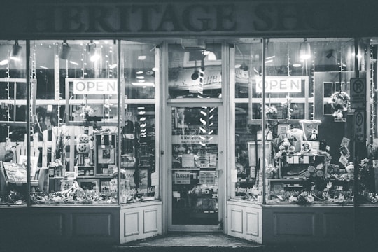 A shopfront with large glass windows showing various items on display. The entrance is adorned with signs indicating 'OPEN' and a variety of goods and decorations can be seen inside, including flowers, wreaths, and other decorative pieces.