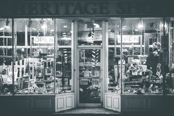 A shopfront with large glass windows showing various items on display. The entrance is adorned with signs indicating 'OPEN' and a variety of goods and decorations can be seen inside, including flowers, wreaths, and other decorative pieces.