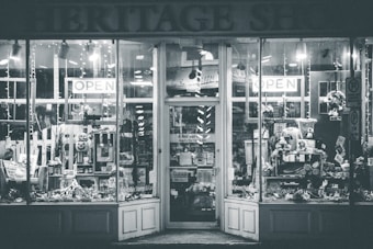 A shopfront with large glass windows showing various items on display. The entrance is adorned with signs indicating 'OPEN' and a variety of goods and decorations can be seen inside, including flowers, wreaths, and other decorative pieces.