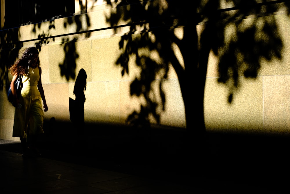 a woman walking down a sidewalk next to a tree