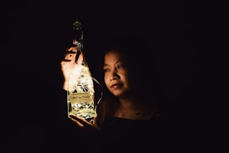 A serene woman holding a glowing moon-shaped elixir bottle in a peaceful natural setting.