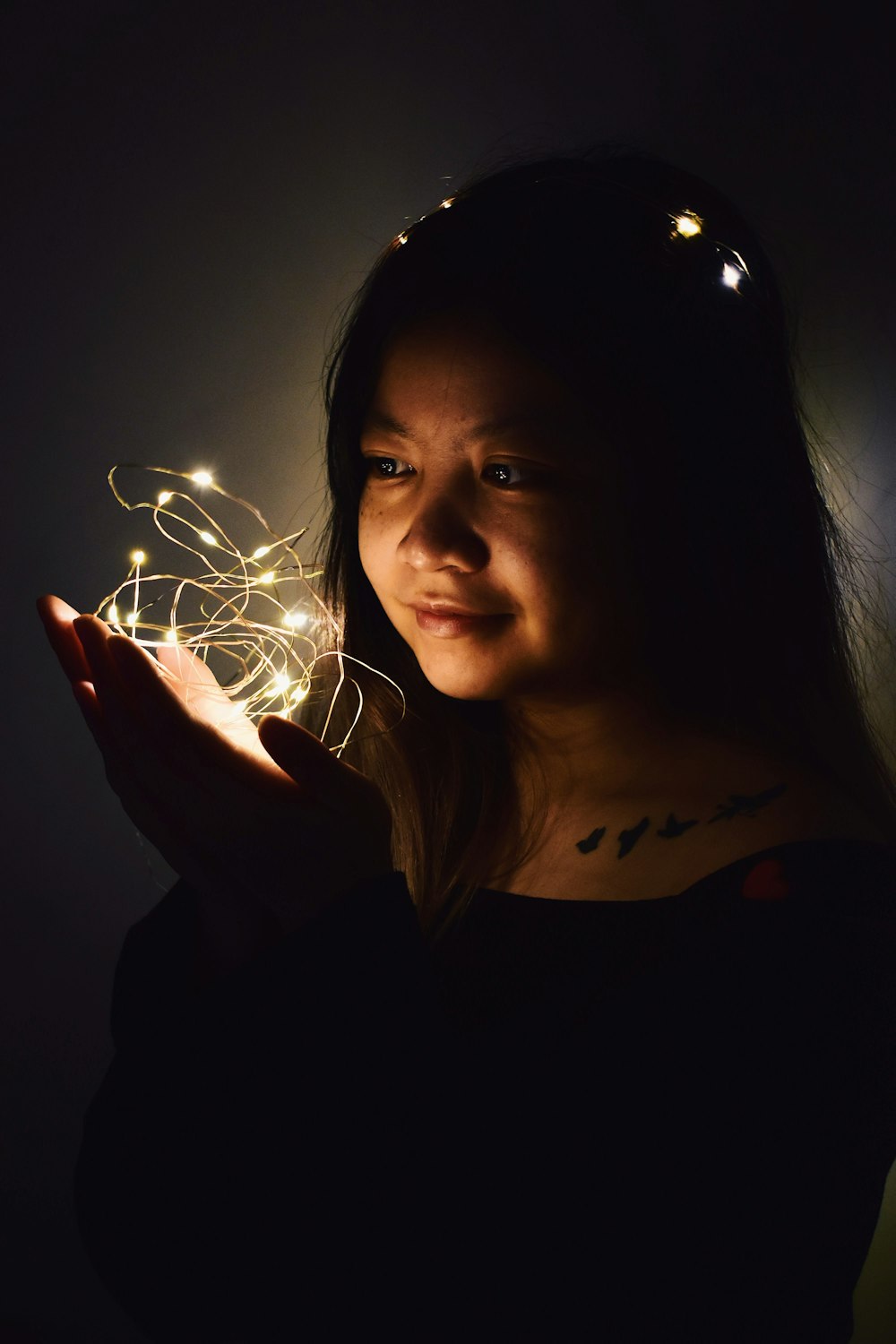 mulher que segura as luzes da corda no quarto escuro