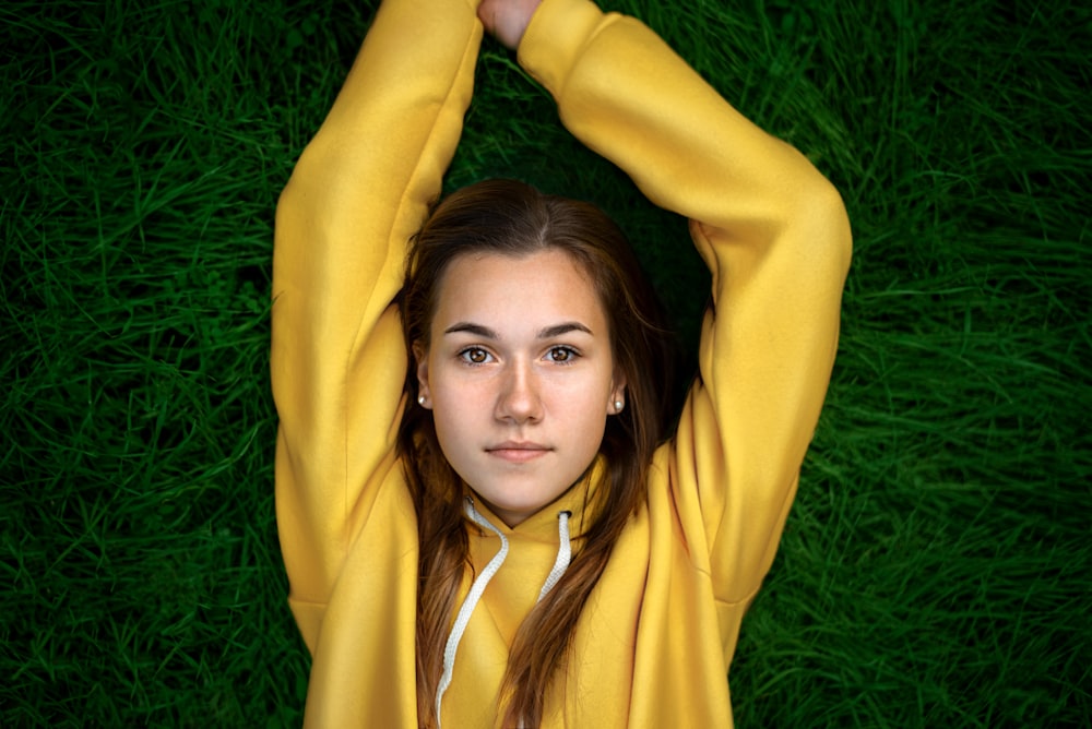 woman in yellow long sleeve shirt lying on green grass