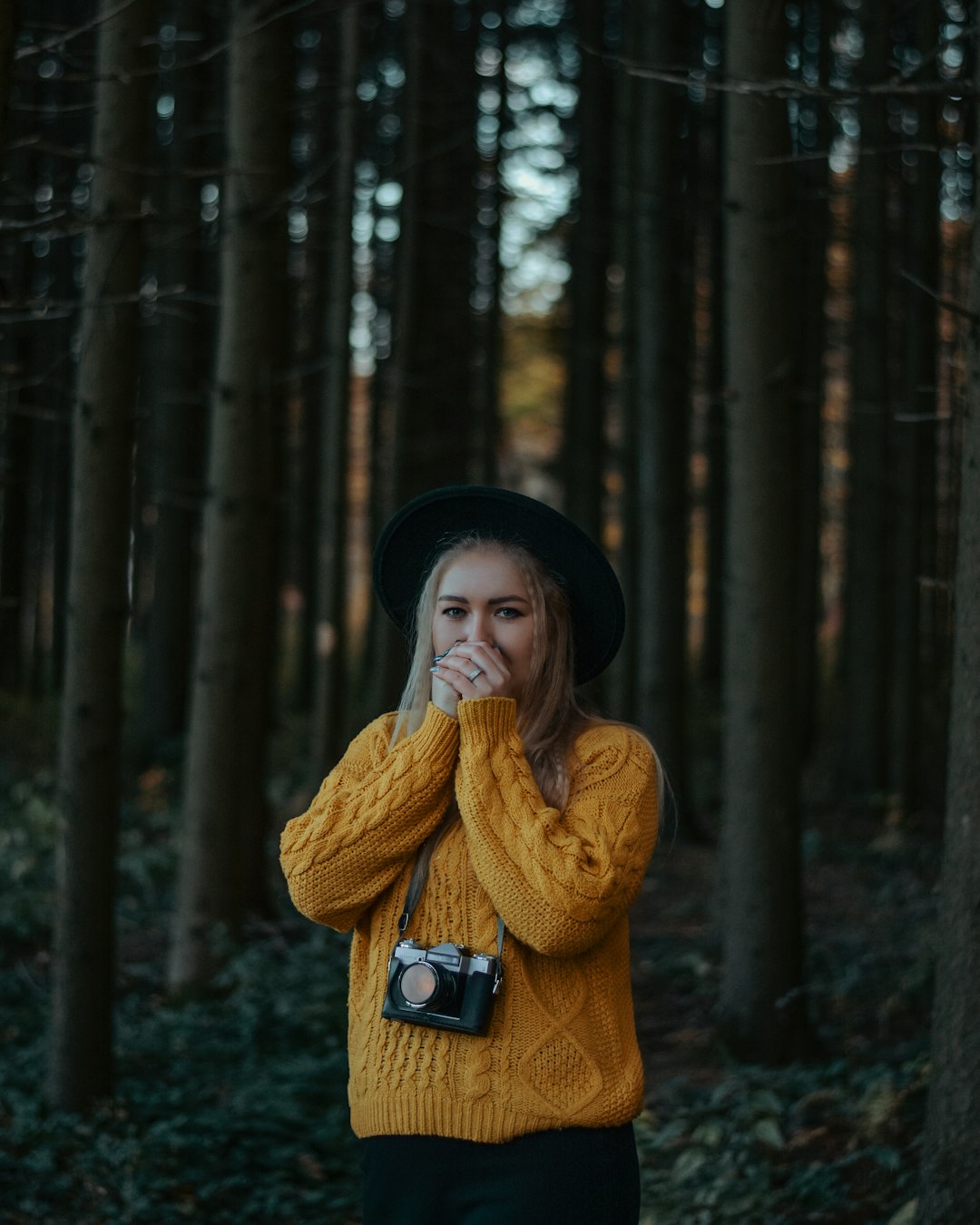 woman in brown knit sweater and black hat standing in forest during daytime