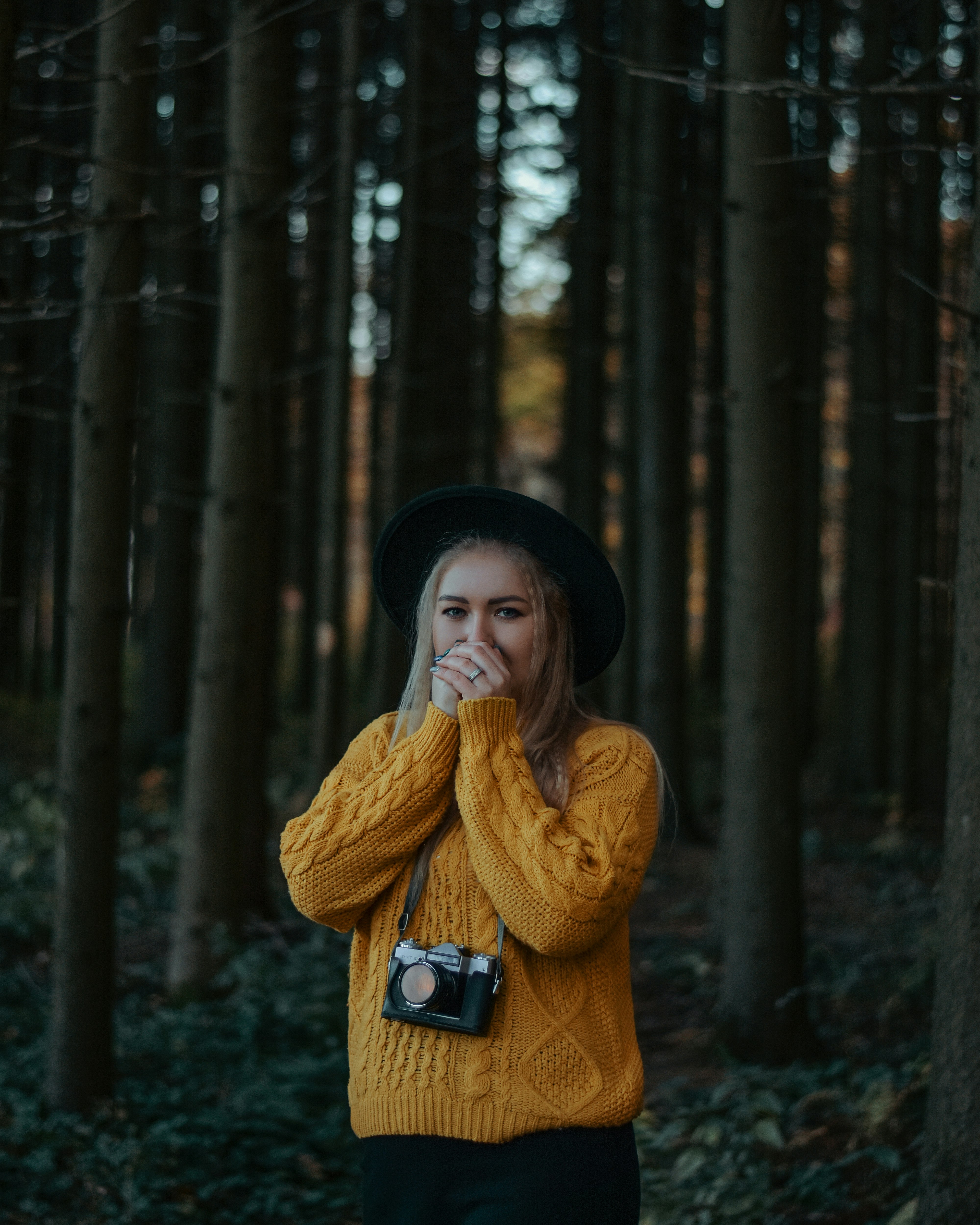 woman in brown knit sweater and black hat standing in forest during daytime