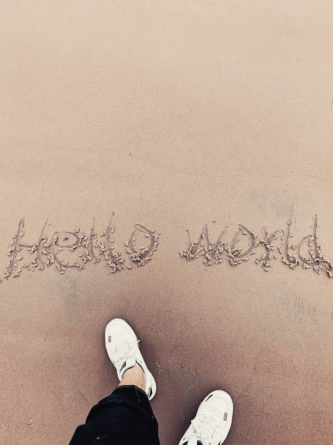 person in white sneakers standing on brown sand