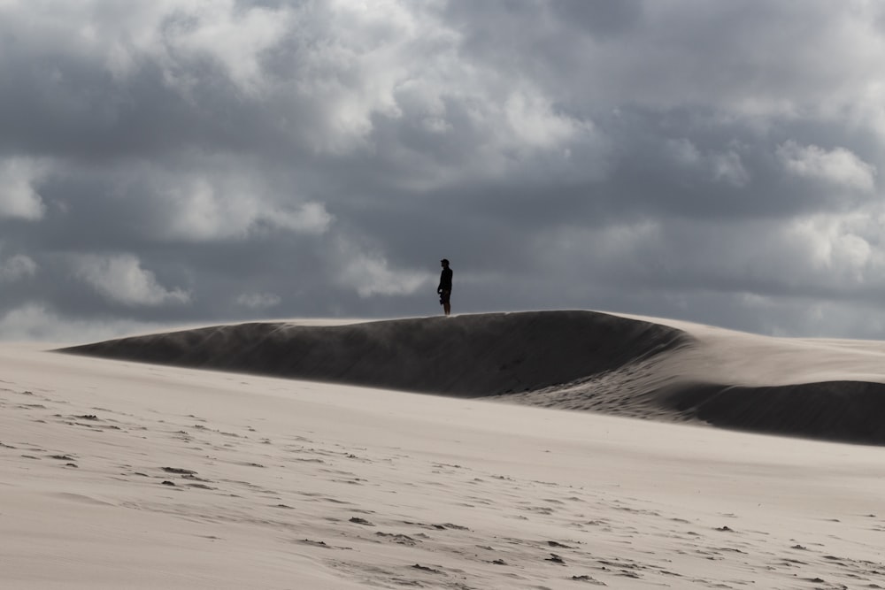 person walking on white sand under white clouds during daytime