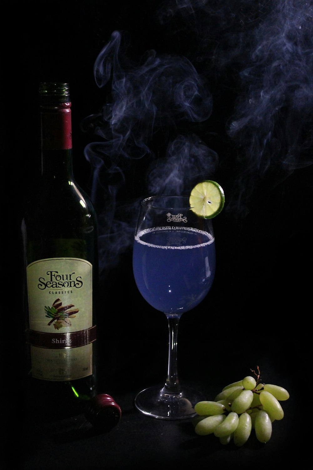 green wine bottle beside wine glass with purple smoke