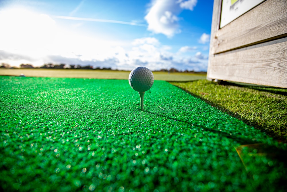 pallina da golf bianca sul campo in erba verde sotto il cielo blu durante il giorno