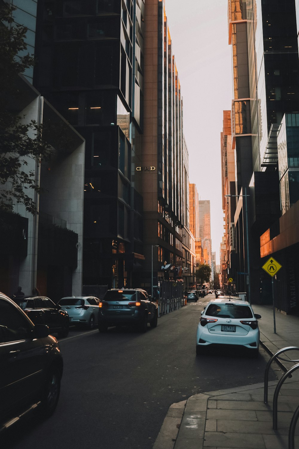 cars parked on side of the road in between high rise buildings during daytime