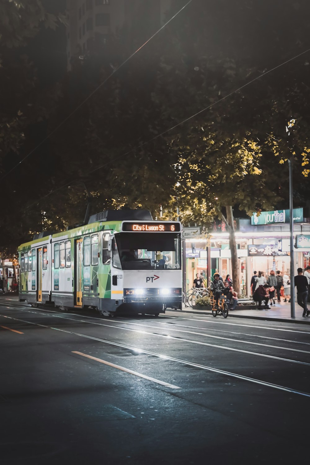 Gente caminando por la calle cerca del tranvía verde y blanco durante la noche