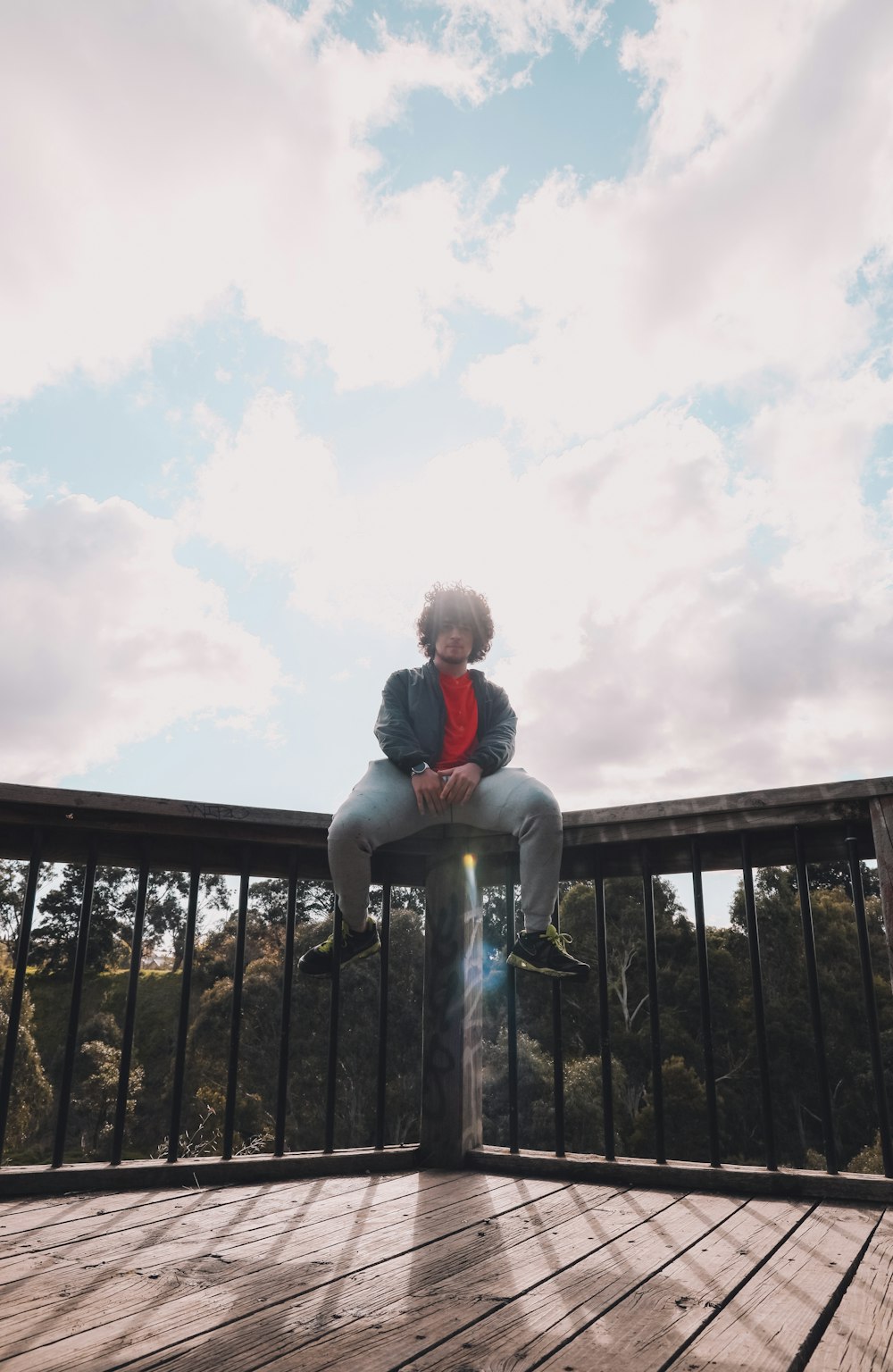 woman in gray jacket sitting on black wooden fence during daytime