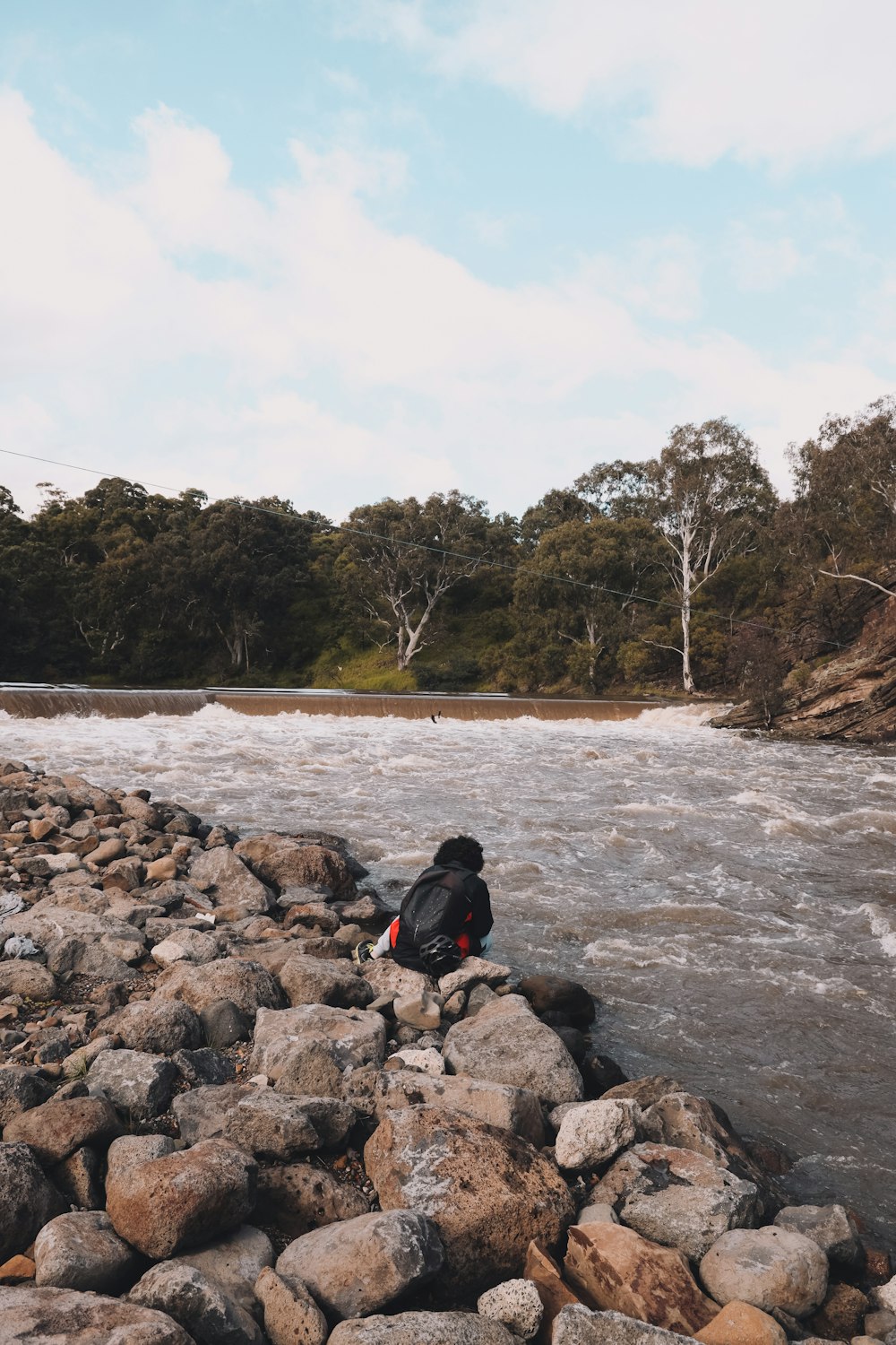 Hombre con chaqueta negra sentado en la roca cerca del cuerpo de agua durante el día