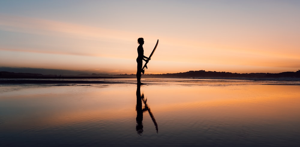 silhouette of man standing on shore during sunset