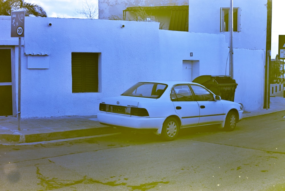 sedã amarelo estacionado ao lado de edifício de concreto azul durante o dia