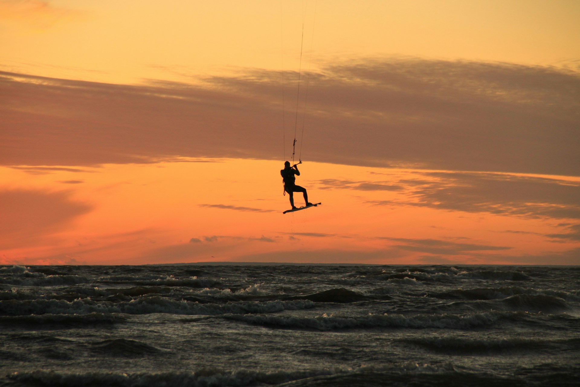 person in black wetsuit surfing on sea waves during sunset