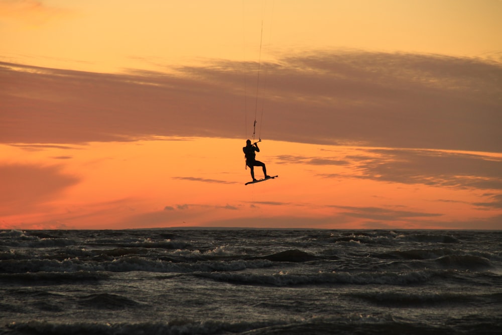 Persona con traje de neopreno negro surfeando en las olas del mar durante la puesta del sol