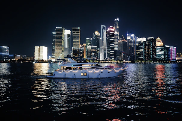 A sleek yacht cruising past Singapore's impressive skyline under a clear twilight sky