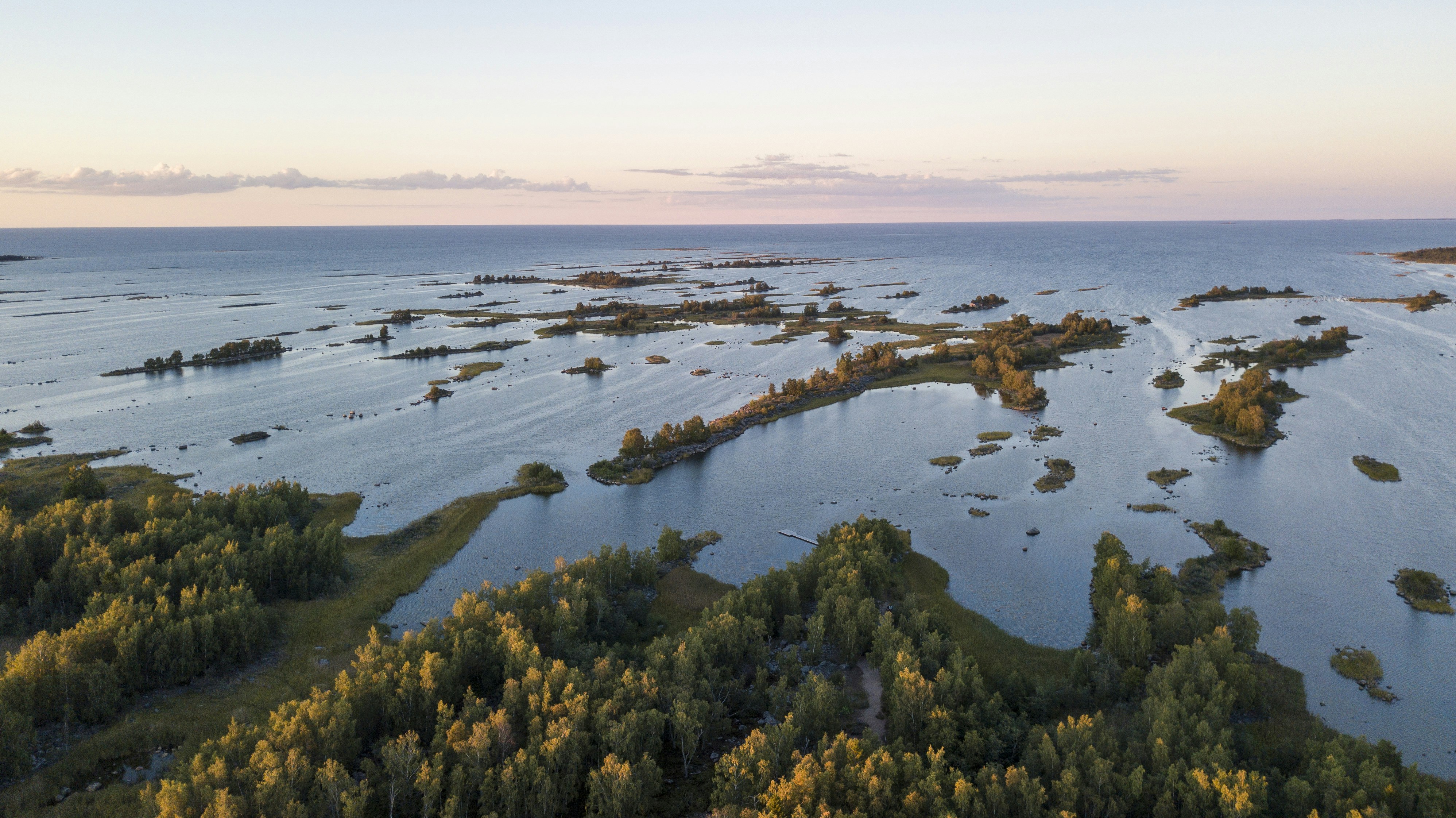 green grass and trees near body of water during daytime, The only Natural UNESCO World Heritage Site in Finland, the Kvarken Archipelago, on a late August trip during Sunset.