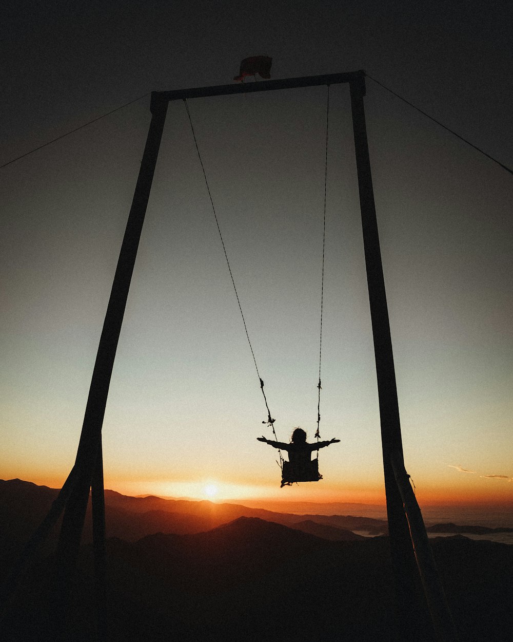 Silhouette der Person, die bei Sonnenuntergang auf Schaukel reitet