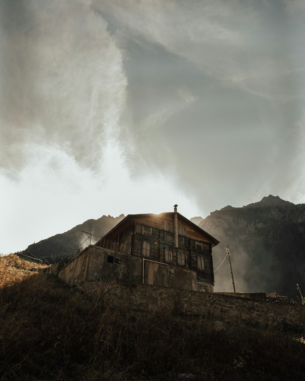 brown wooden house near mountain under white clouds during daytime