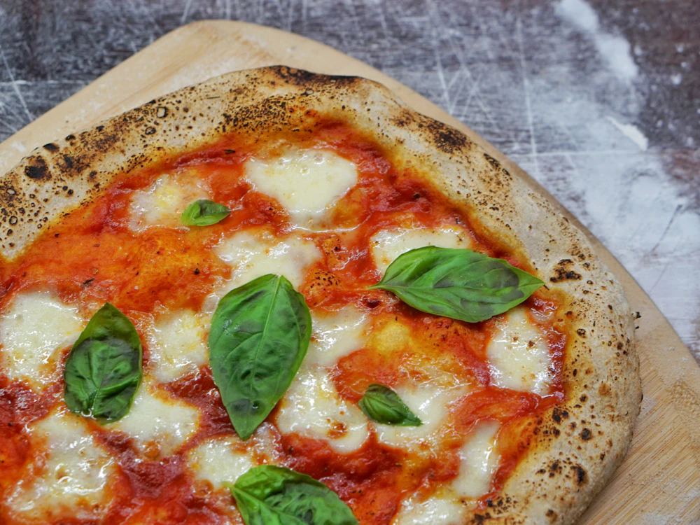 A margherita with a leopard-spotted crust on a scarred wooden peel, basil leaves on top