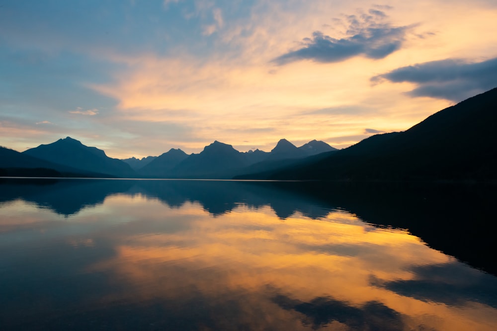 body of water near mountain under cloudy sky during daytime