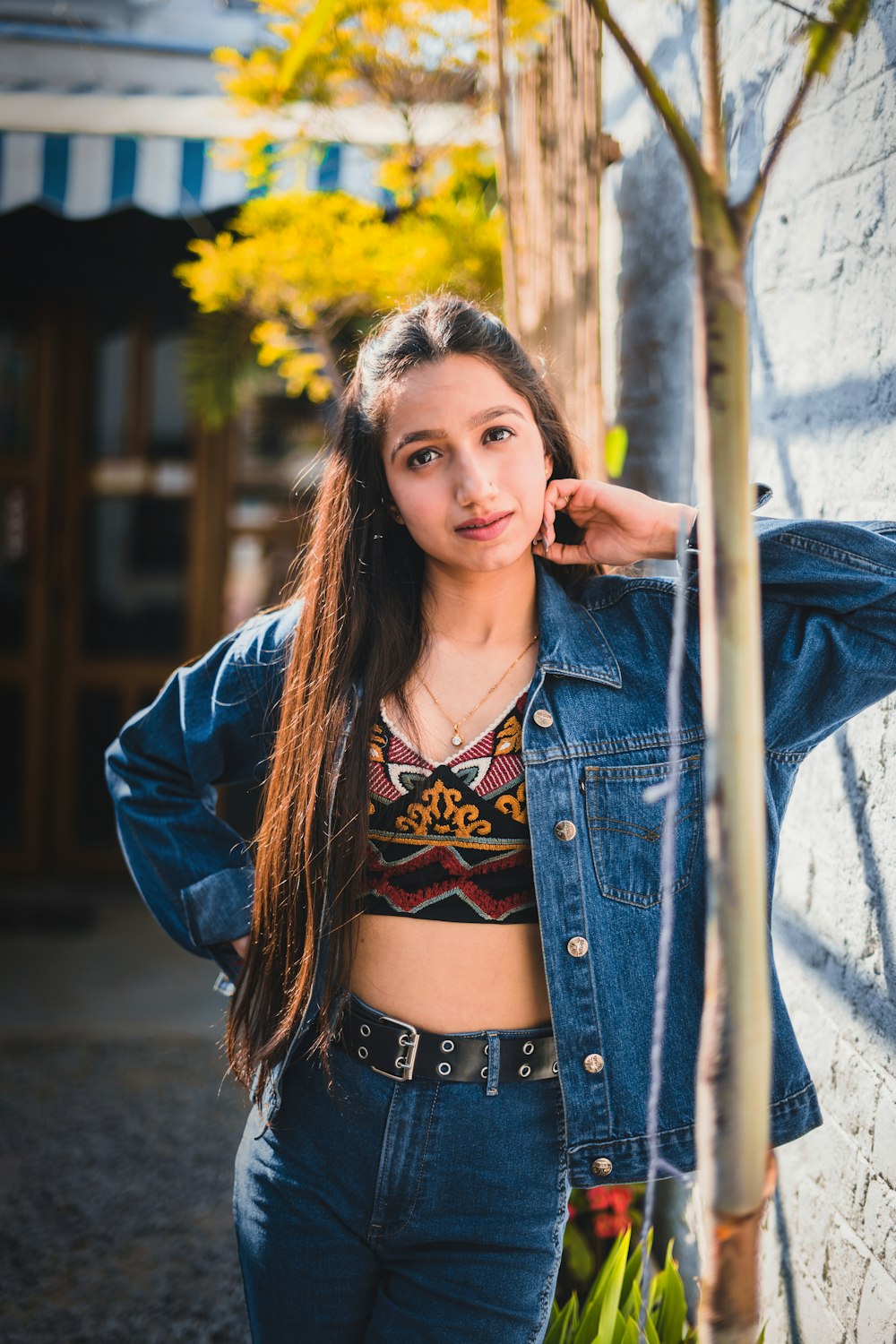 woman in blue denim jacket standing and leaning on brown wooden post during daytime