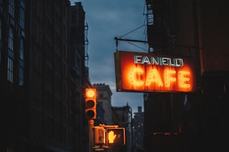 A vibrant neon box sign glowing brightly outside a cozy cafe at dusk.