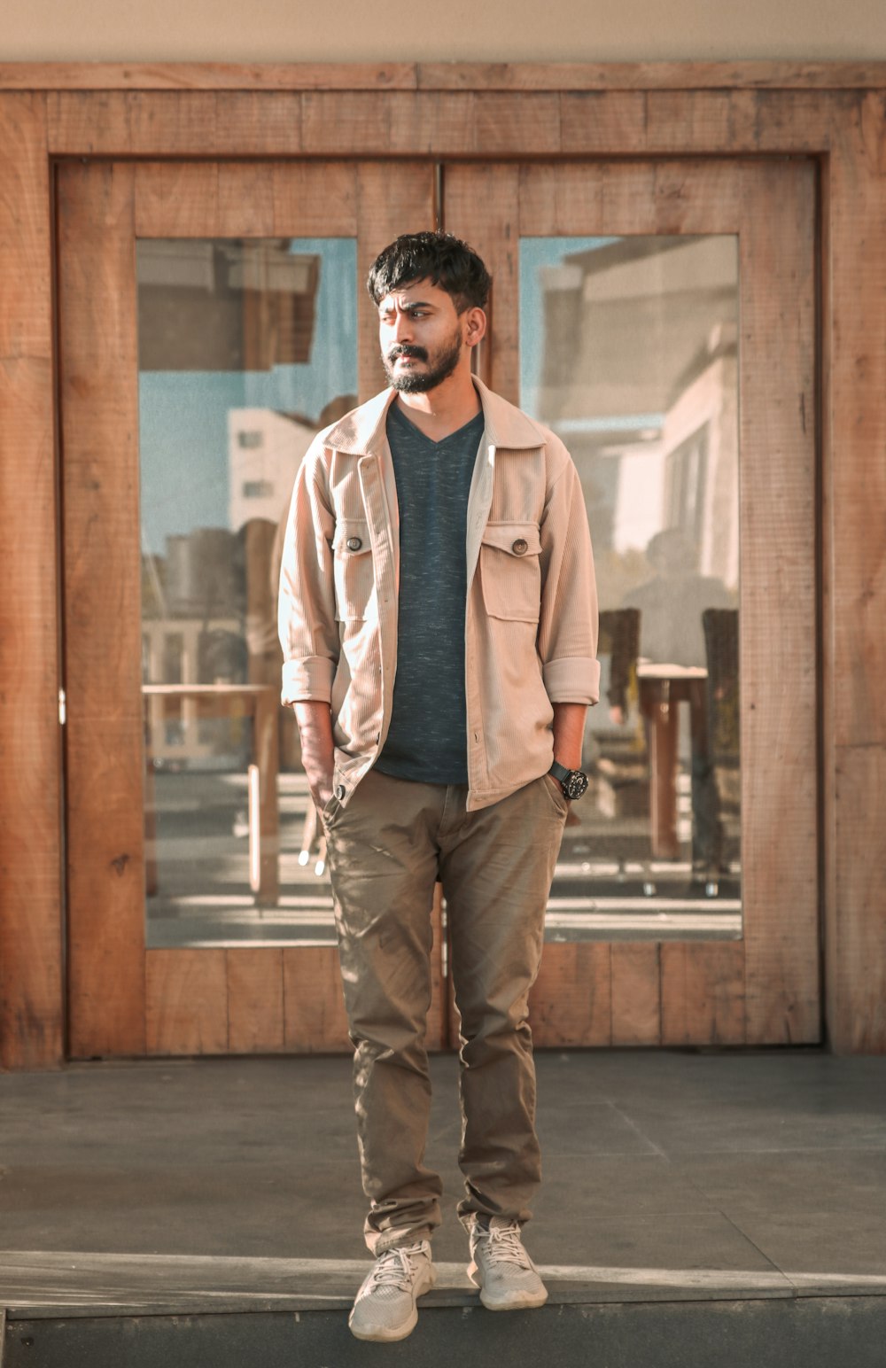 Homme en chemise blanche et jean bleu debout à côté d’un mur en bois brun pendant la journée