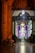 A warmly lit, ornate doorway opens into a church interior, where a congregation gathers near a brightly illuminated altar. An elderly person in a wheelchair sits on the left side of the entrance.