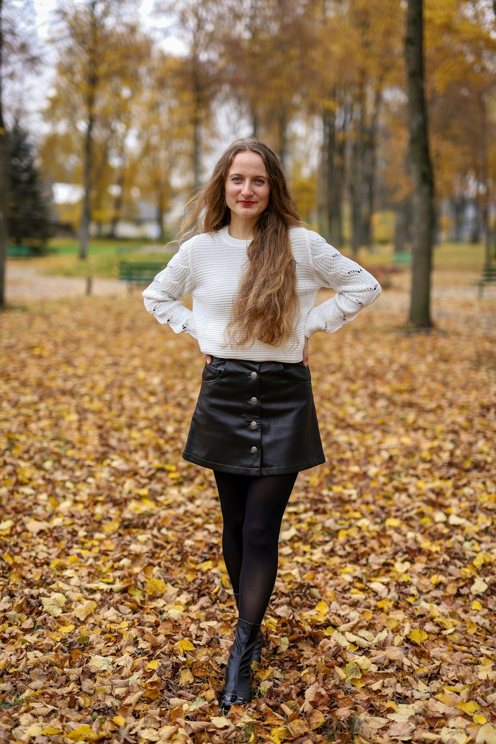 woman in white long sleeve shirt and black skirt standing on yellow leaves during daytime