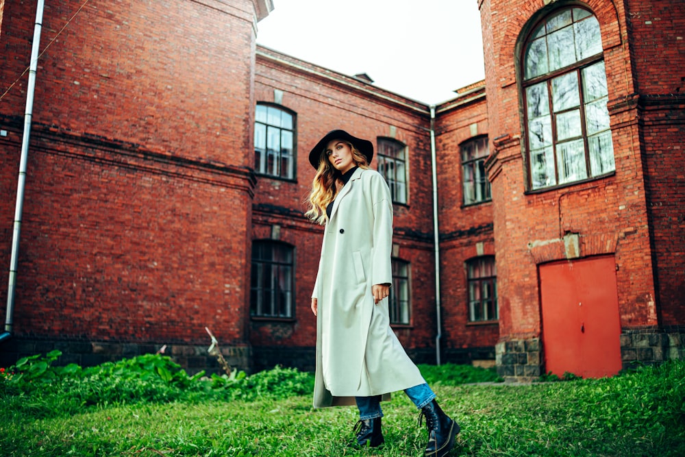 woman in white coat standing near brown brick building