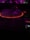 A DJ controller with illuminated buttons in a dark setting featuring a prominently glowing turntable surrounded by a red light. The background is blurred with hints of purple and magenta lights.