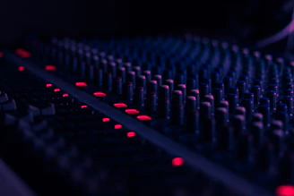 Close-up of a mixing console with glowing knobs and sliders in a dimly lit studio.