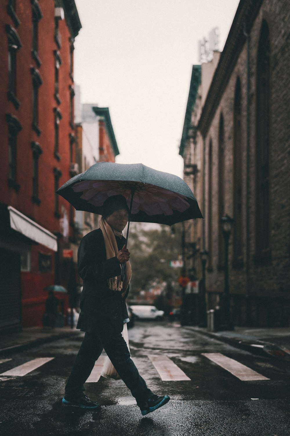 Mann in schwarzer Jacke mit Regenschirm geht tagsüber auf der Straße