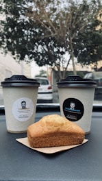A delivery person handing a fresh fruit and a cup of coffee to a traveler beside a taxi on a highway rest stop.