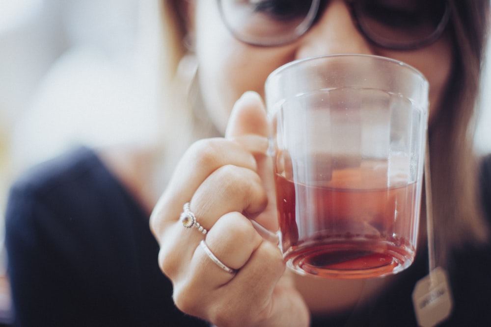 woman holding clear drinking glass with red liquid