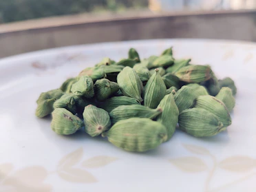 Close-up of vibrant green cardamom pods resting on a rustic wooden surface with Kerala hills blurred in the background.