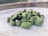A close-up image of several green cardamom pods placed on a white surface, possibly a plate. The background is blurred, drawing attention to the cardamom pods in the foreground.
