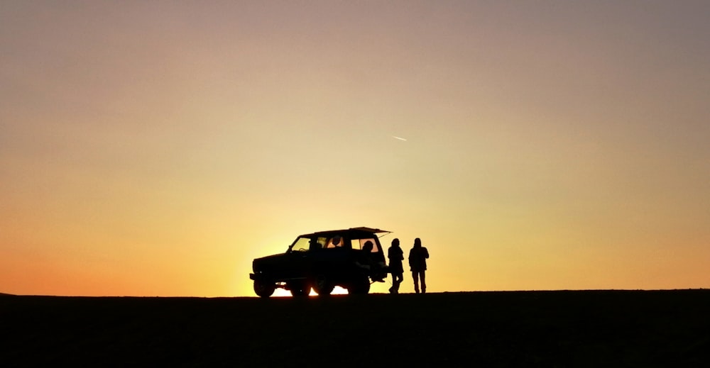 silhouette of 3 men standing beside car during sunset